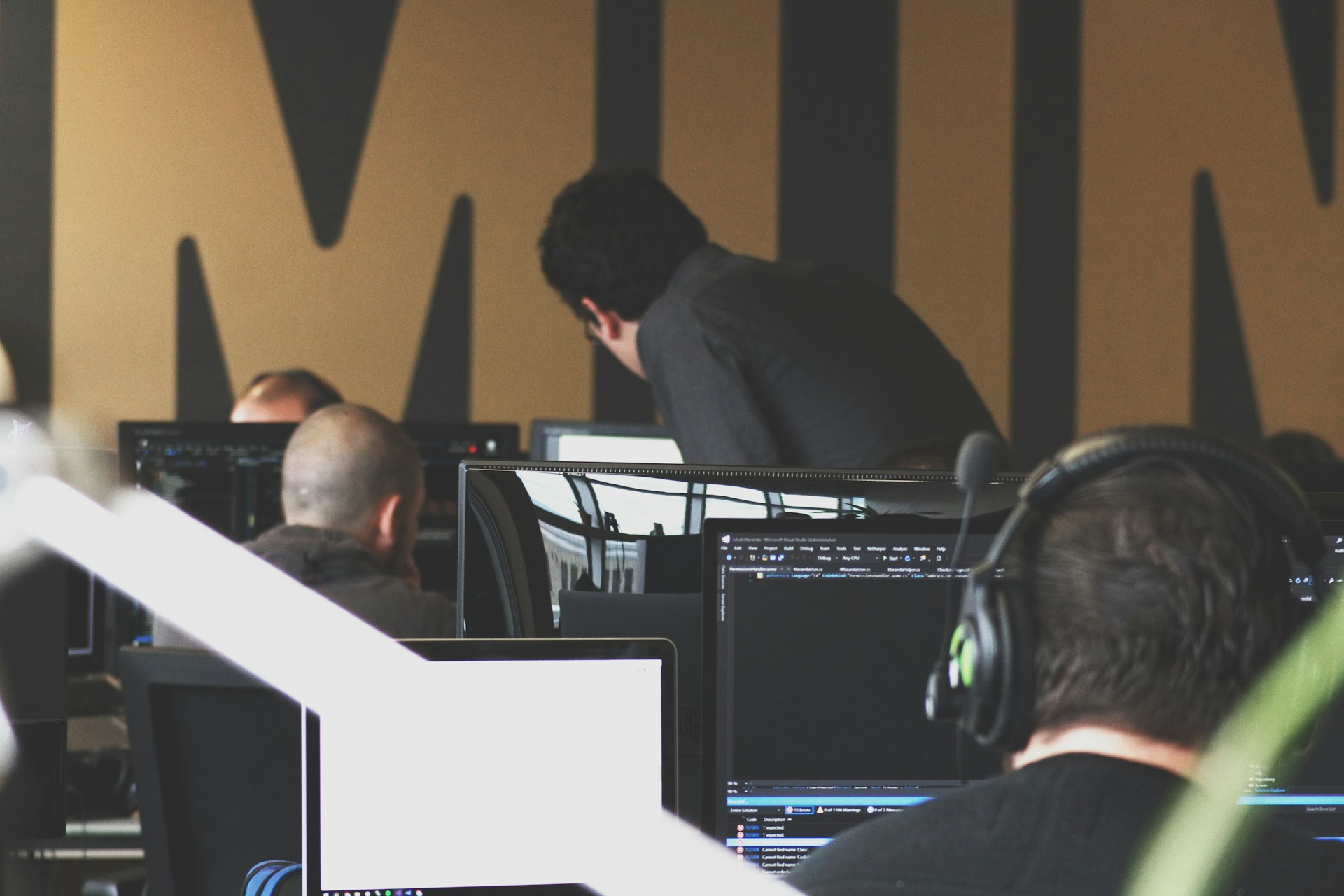 Photo of an office space with multiple workers using their monitors, with a supervisor looking over an employee's work